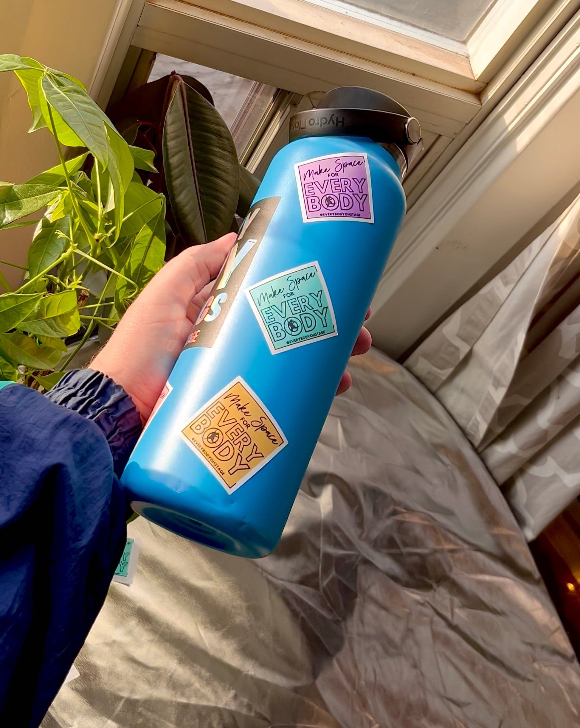 a blue water bottle with colourful stickers that say "Make space for EveryBODY" with the @EveryBODYonStage tag at the bottom.
